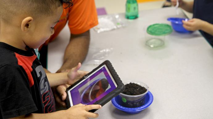 A preschool boy taking a photograph of a container of dirt with the app.