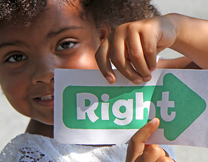 A young girl holds up a paper arrow with the word “Right” written on it.