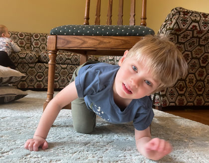 A young boy climbs out from under a chair.