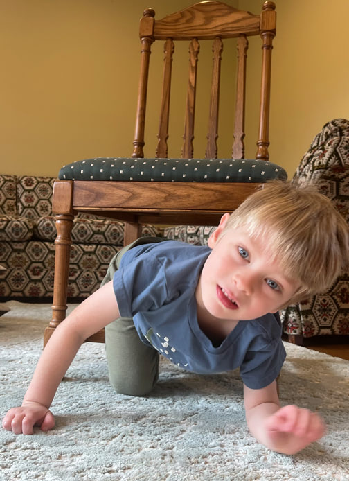 A young boy climbs out from under a chair.