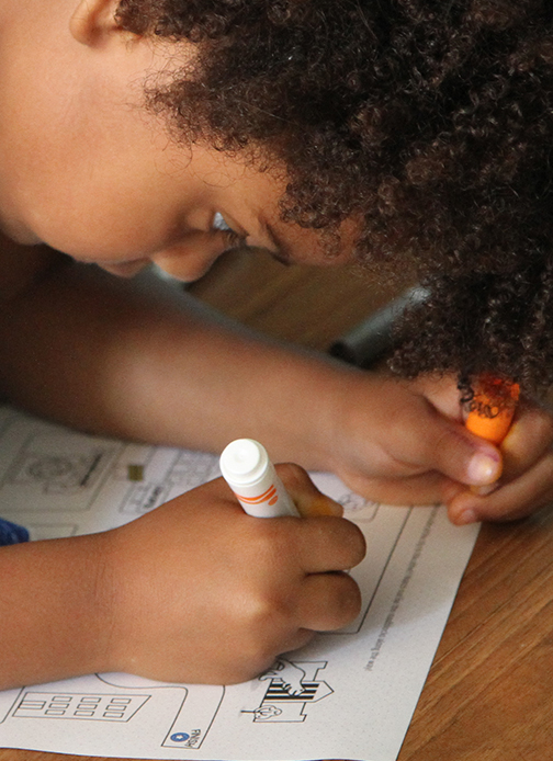 A young girl uses a marker as she navigates a maze on paper.