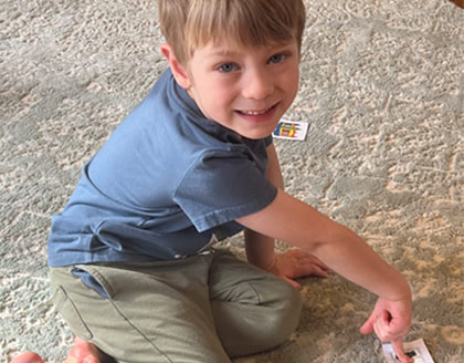 A young boy sits on the floor and points to a printed out picture of a fair landmark with other landmark pictures around him.