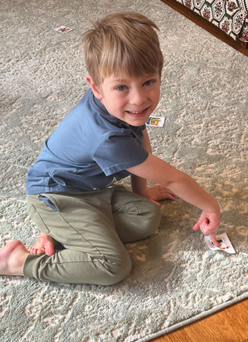 A young boy sits on the floor and points to a printed out picture of a fair landmark with other landmark pictures around him.