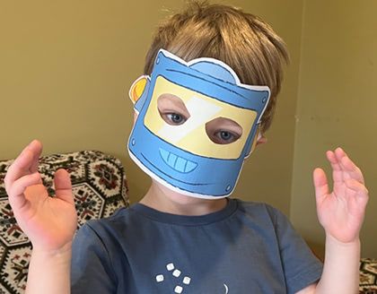 A young boy wears a printed out blue robot mask.