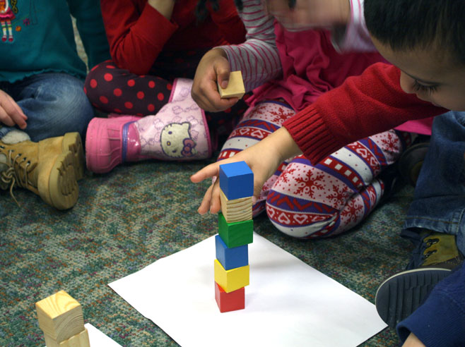 A child reaches out to straighten the block tower he is building.