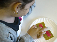 A girl points to paper berries on pretend waffles to count them.