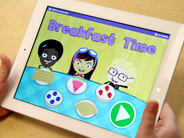 Close-up of a child’s hands holding an iPad that shows the home screen of the Gracie and Friends Breakfast Time app.