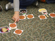 Close-up of a teacher’s hand pointing to paper cut-outs of three Gracie and Friends characters and six cookies spread out on the floor.