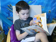 A preschool boy sits in a chair and turns a page in the book The Doorbell Rang.