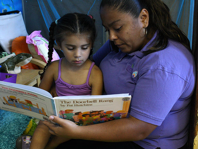 A teacher reads The Doorbell rang to a young girl sitting in her lap.
