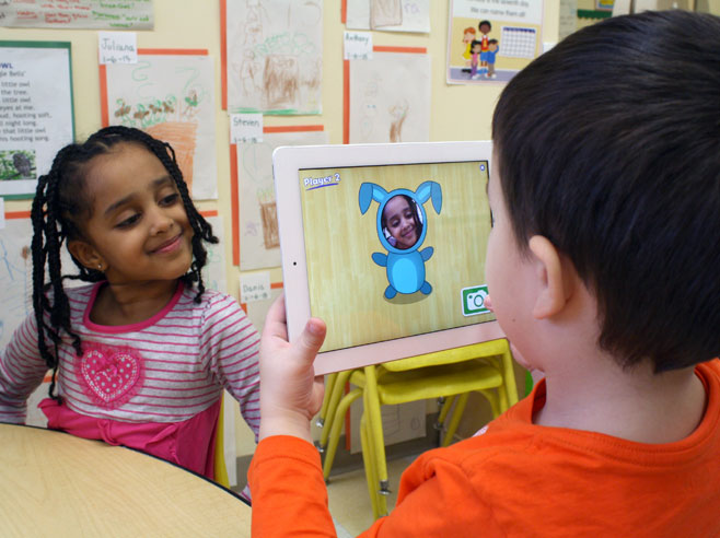 A young boy takes a photo of a girl in a striped shirt. Her face appears on-screen as part of a blue bunny.