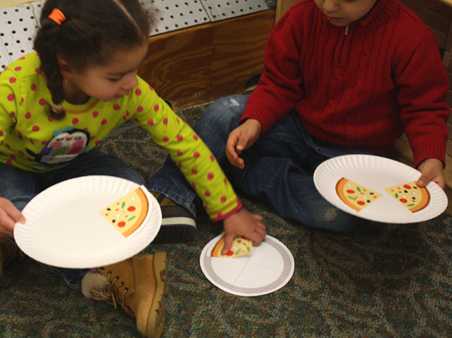 Two children divide pieces of paper pizza equally between two paper plates.