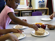 A girl reaches out to take a rice cake from a plate on a table. Other plates of snacks are nearby.