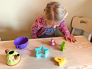 A girl looks at a table at differently-shaped objects from above.