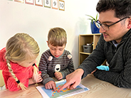 A man points to a map of the United States of America on a table with a boy and a girl.