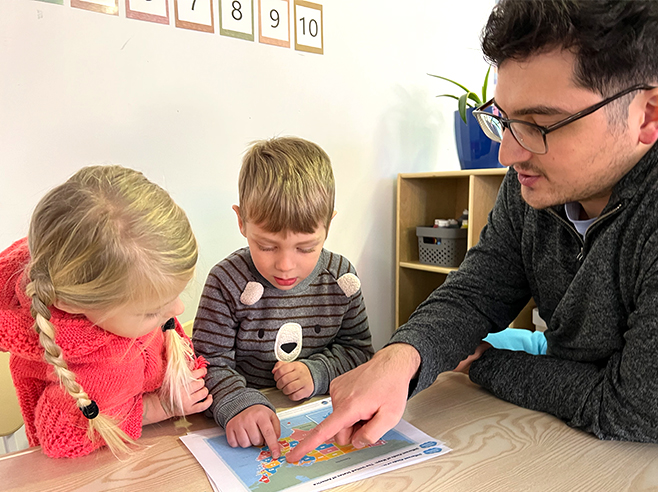 A man points to a map of the United States of America on a table with a boy and a girl.