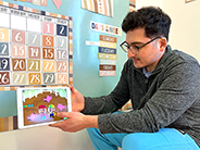 A man models playing a game that shows two characters in a pig pen in the Gracie & Friends “Map Adventures” preschool spatial thinking app.