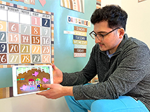 A man models playing a game that shows two characters in a pig pen in the Gracie & Friends “Map Adventures” preschool spatial thinking app.