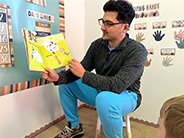A man holds up and reads the book “Piggies in the Pumpkin Patch,” by Mary Peterson and Jennifer Rofé.