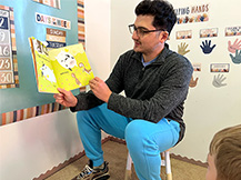 A man holds up and reads the book “Piggies in the Pumpkin Patch,” by Mary Peterson and Jennifer Rofé.