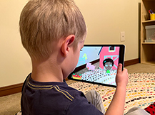 A boy views a digital farm scene through an iPad as he plays the Gracie & Friends “AR Adventures” augmented reality app.