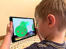 A boy views digital apple trees through an iPad as he plays the Gracie & Friends “AR Adventures” augmented reality app.