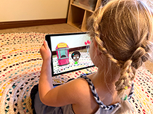 A girl views a digital fair scene through an iPad as she plays the Gracie & Friends “AR Adventures” augmented reality app.