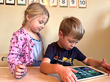 A boy plays the Gracie & Friends “Map Adventures” preschool spatial thinking app while a girl watches.