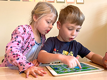 A boy plays the Gracie & Friends “Map Adventures” preschool spatial thinking app while a girl watches.