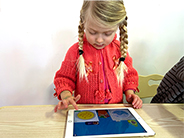 A girl swirls laundry around in digital dryer as she plays the Gracie & Friends “Map Adventures” preschool spatial thinking app.
