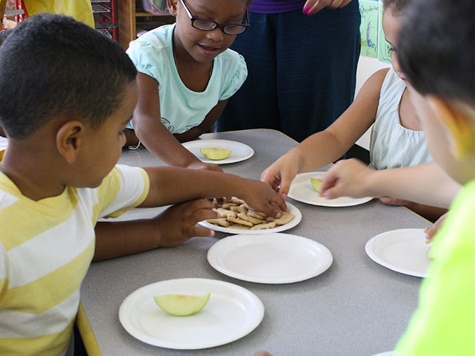 Four young children reach for snacks on a serving plate.
