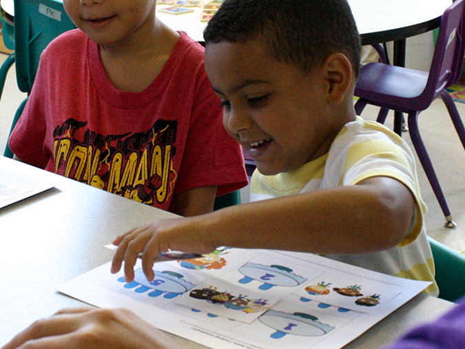 A boy in a yellow striped shirt gleefully places a card on his game board.