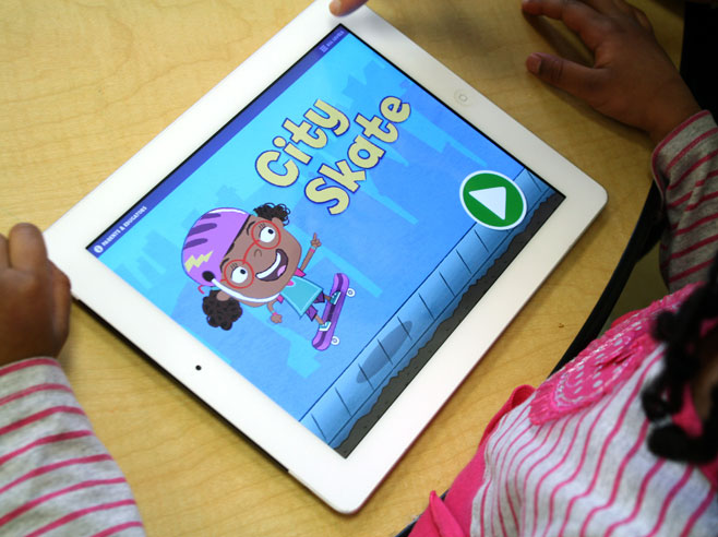 A preschool girl in a pink striped shirt looks at the Gracie and Friends City Skate app on an iPad.