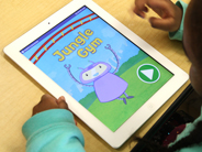 The home screen of the Gracie and Friends Jungle Gym app is seen on an iPad, with a young girl’s hands nearby.