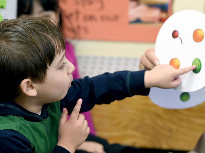 A boy points to one of four fruits on a round paper card.