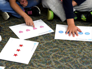 Two children divide pieces of paper pizza equally between two paper plates.