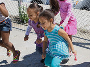 Children hop away from a fence bordering the playground pavement.