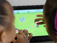 Two preschool girls drag the ends an on-screen rope and catch a bubble in the Gracie and Friends Treasure Bubbles app.