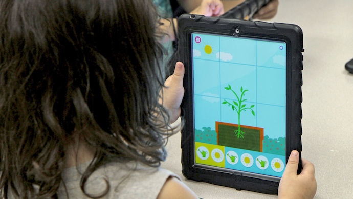 A preschool girl watching a tomato plant grow in the Wonder Farm app.