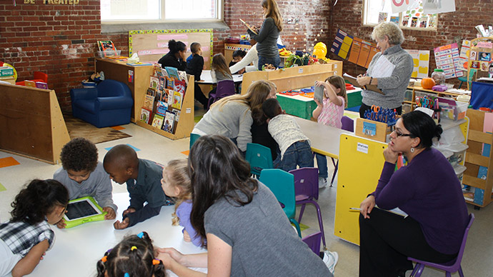 Team members from First 8 Studios at WGBH play with children on tablets in a preschool classroom.