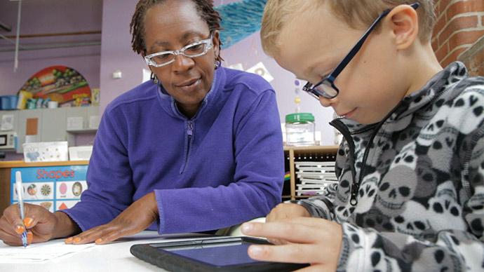 A First 8 Studios at WGBH team member takes notes as she watches a young boy play on an iPad.