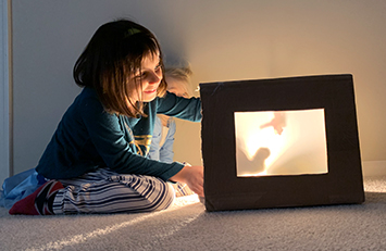 Child makes shadows in a shadow box theater.