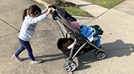 Child pushing a stroller up a driveway ramp.