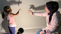 Parent and child making shadows on the wall with their hands.