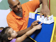 Teacher helps student point to picture cards on a board.