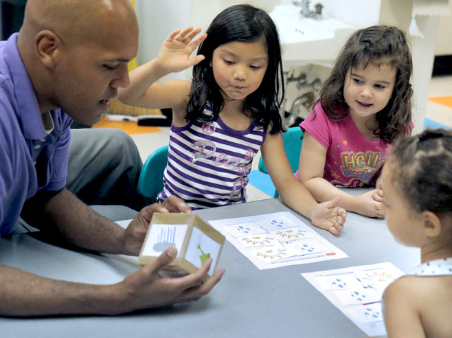 Teacher looks at pictures on dice and engages with group of students.