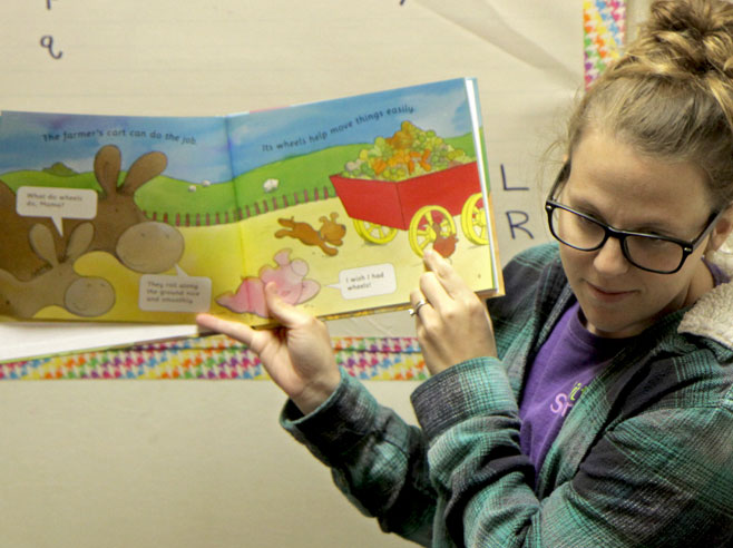 Teacher holds up opened book and looks down at students.