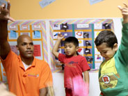 Students and teacher hold hands in the air, during a song about gravity.