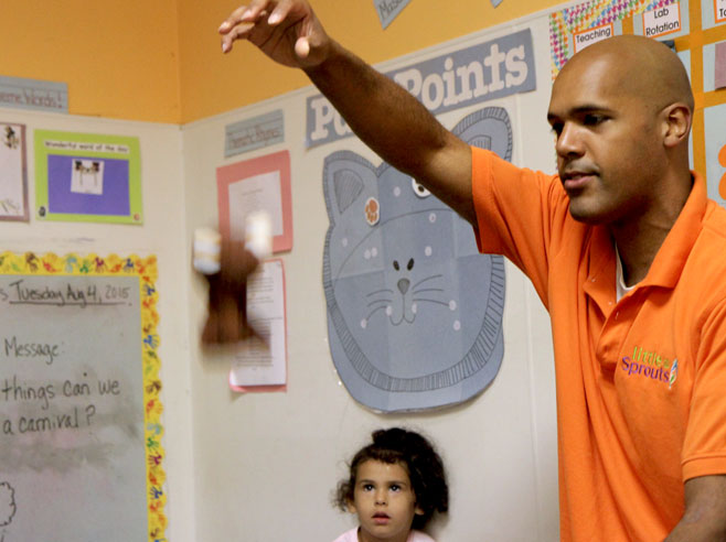 Teacher holds his hand in the air, during a song about gravity.
