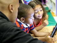 Two students and a teacher, at a table, looking at an iPad.